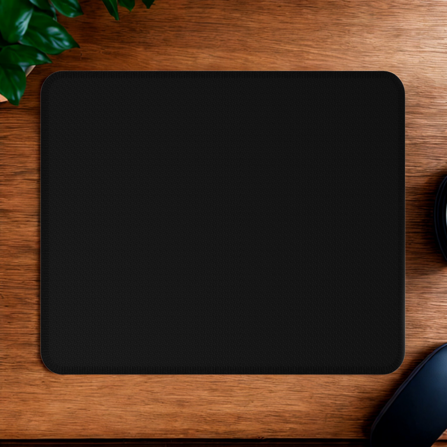 Back of mouse pad on a wooden desk with a plant and computer mouse.