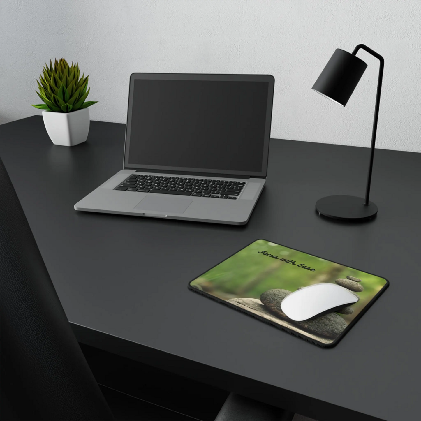 Laptop on a desk with a mouse pad featuring nature design, lamp, and plant.