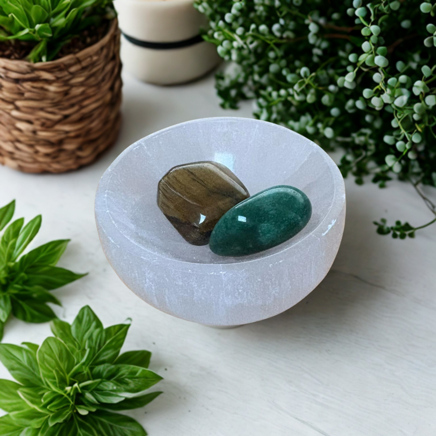Selenite bowl with tumble stones placed on a textured surface with plants in the background.