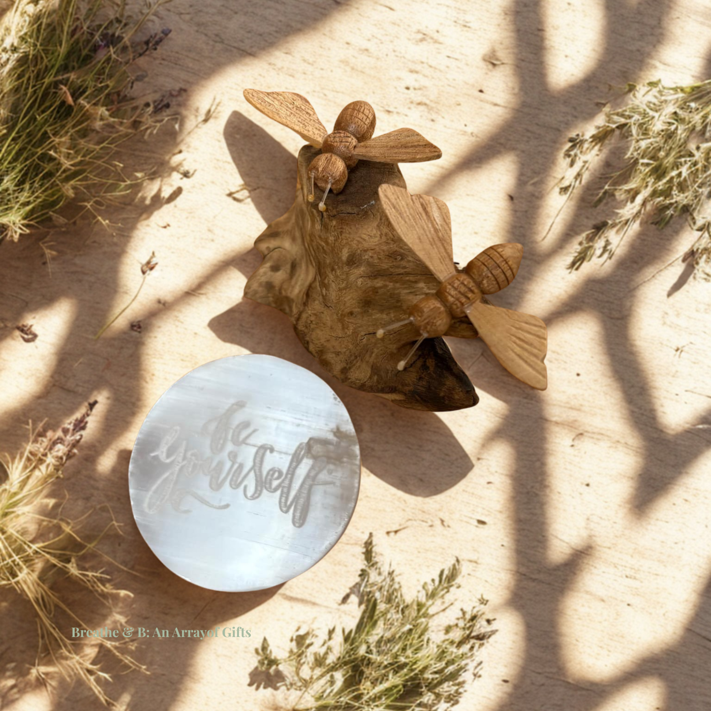 Selenite charging plate with 'be yourself' text with driftwood with 2 bees on a sandy surface with natural elements