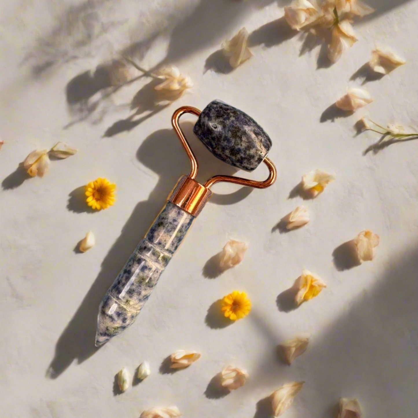 Sodalite crystal facial roller on a light surface with dried flowers