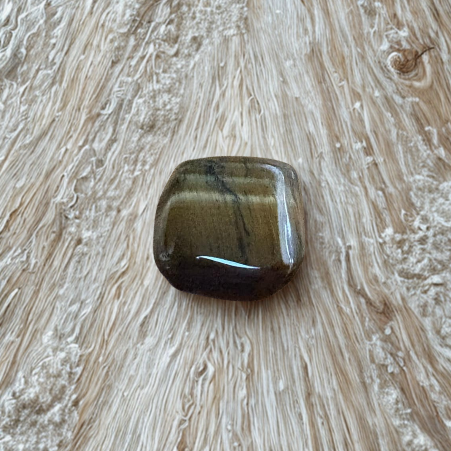 Tigers Eye Tumble Stone on a textured wooden surface