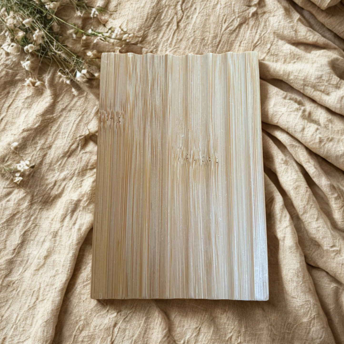Wooden soap dish on a textured beige surface with dried flowers.