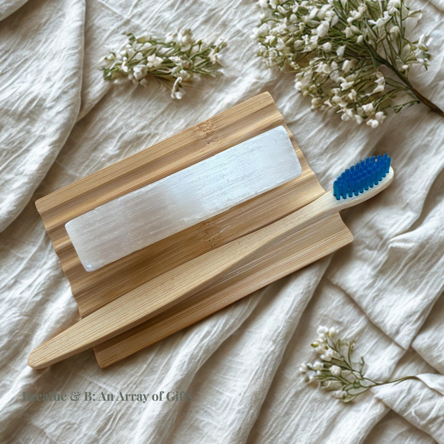 Wooden soap dish with adult bamboo toothbrush and selenite rod on a beige fabric background with small flowers.