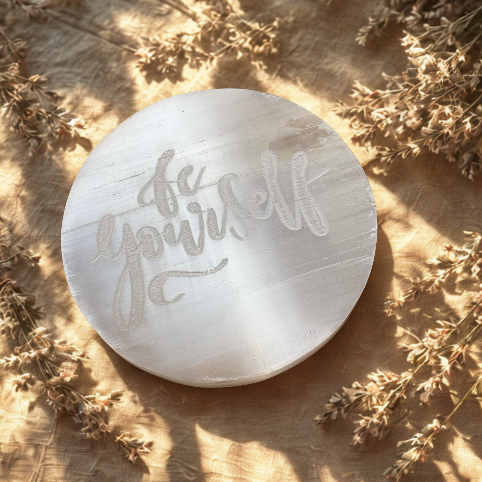 Round stone with 'Be yourself' engraving on a wooden surface with dried plants.