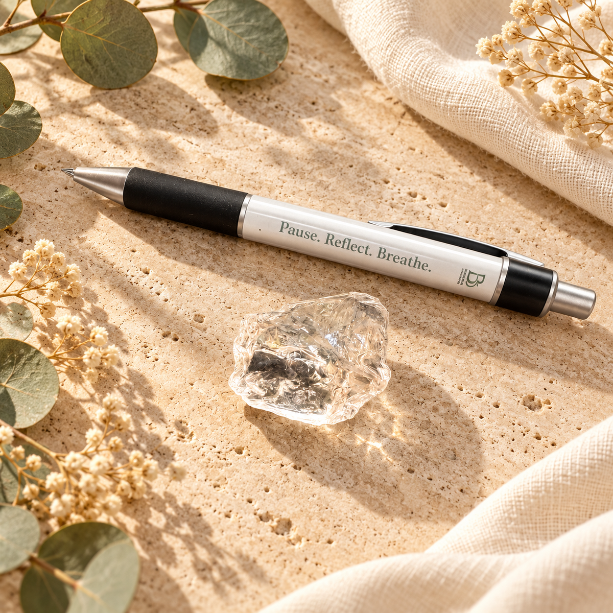 Breathe and B Pause Reflect Breathe pen displayed beside a small natural raw clear quartz cluster on warm travertine.