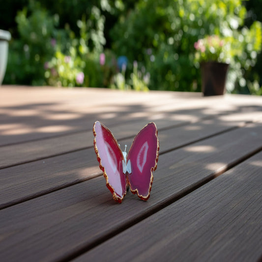 Pink Agate butterfly sculpture on a wooden deck with blurred scenery
