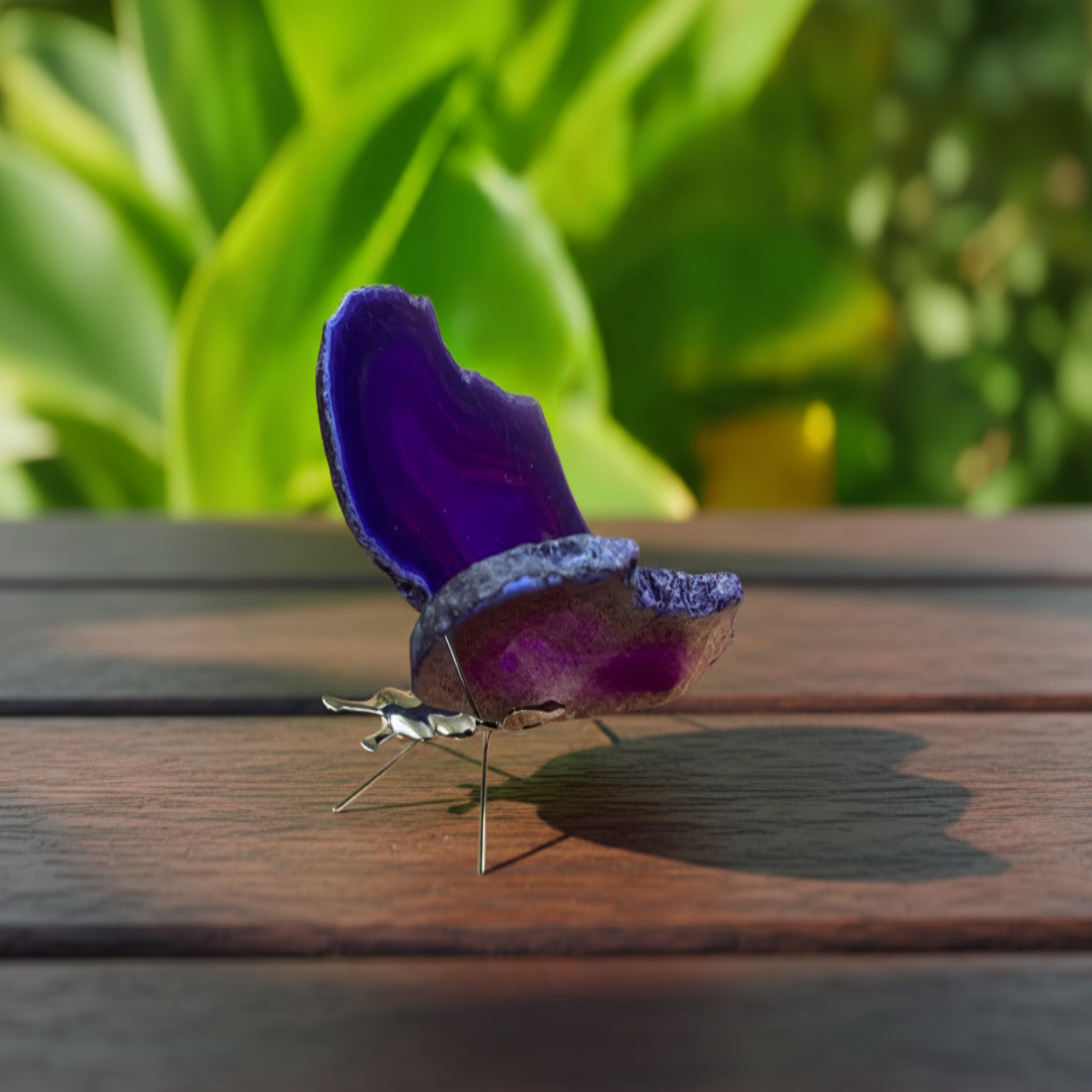 Purple butterfly-shaped object on a wooden surface with green foliage in the background