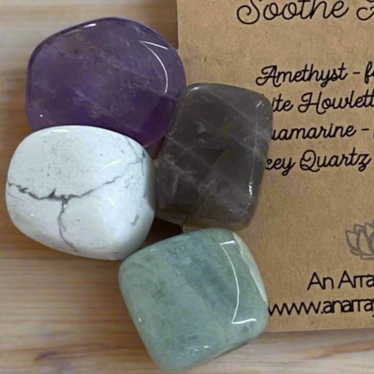 Four tumbled gemstones on a wooden surface with a branded card in the background.