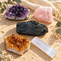 Five-piece crystal kit featuring amethyst, citrine, rose quartz, raw black tourmaline and a white selenite rod on a warm neutral surface.