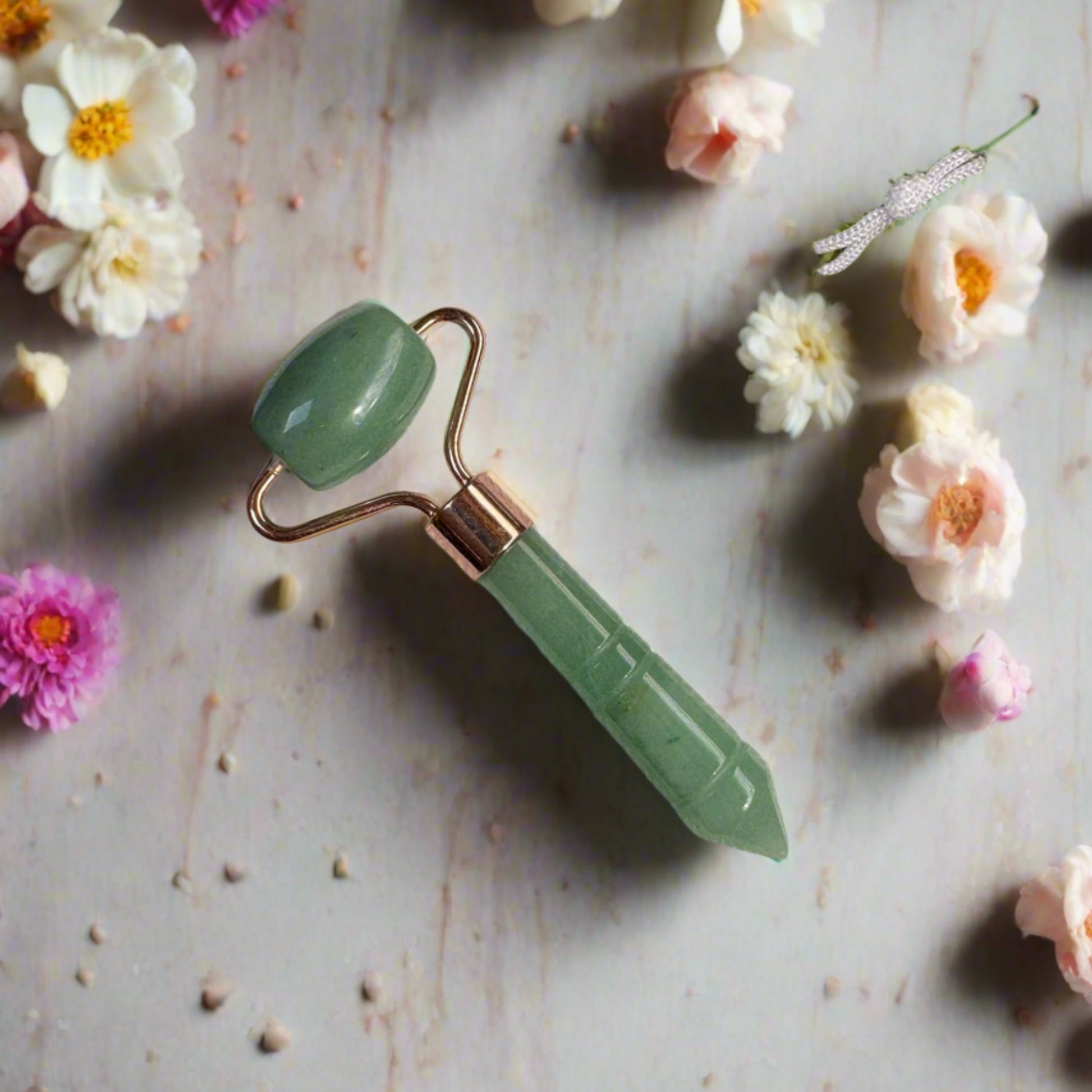 Green jade roller on a textured surface with flowers around