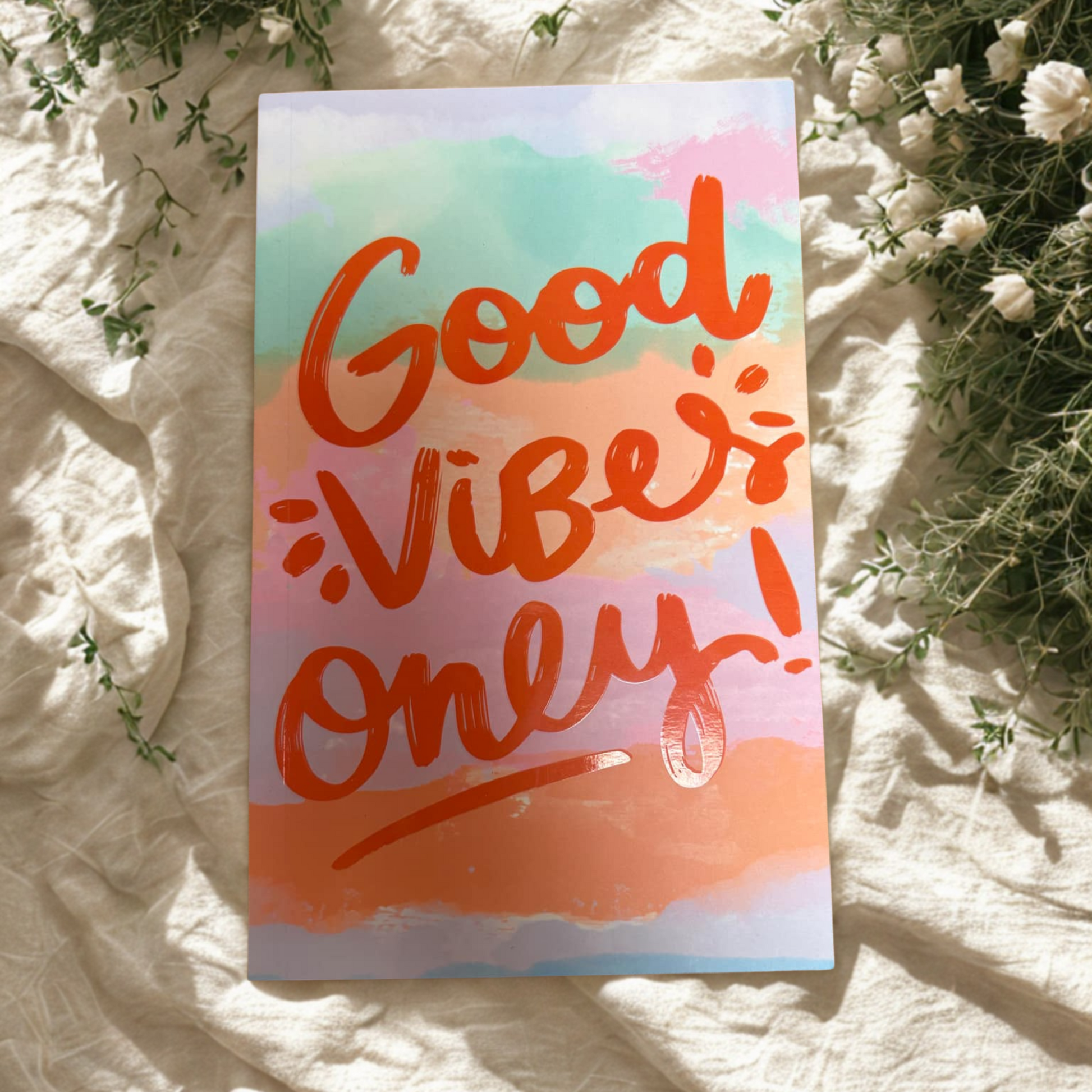 Notebook 'Good Vibes Only!' text on a pastel gradient background, surrounded by white flowers and greenery.