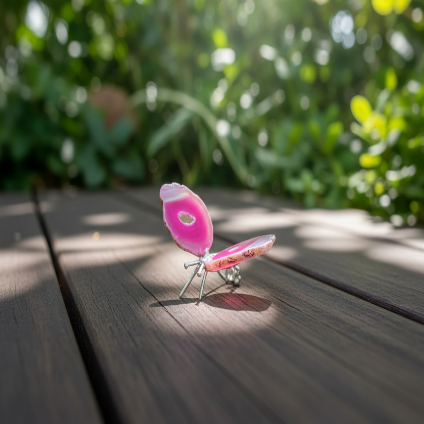Pink agate butterfly on a wooden surface with greenery in the background