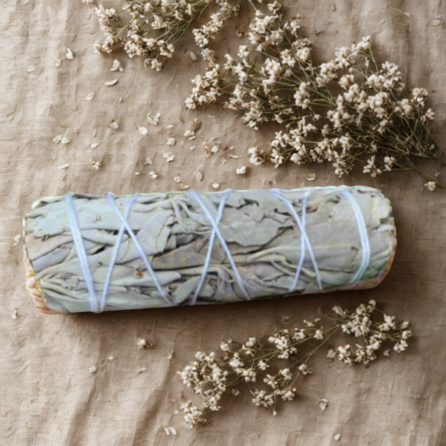 Rolled sage bundle tied with twine on a beige fabric background with small white flowers.