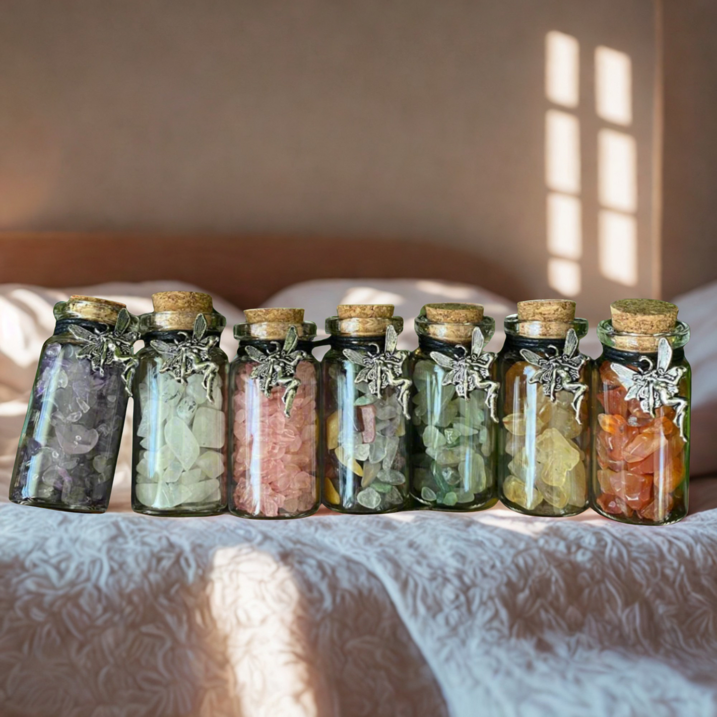 Row of glass jars with cork lids with crystal chips and fairy charms on a textured surface with sunlight casting shadows.