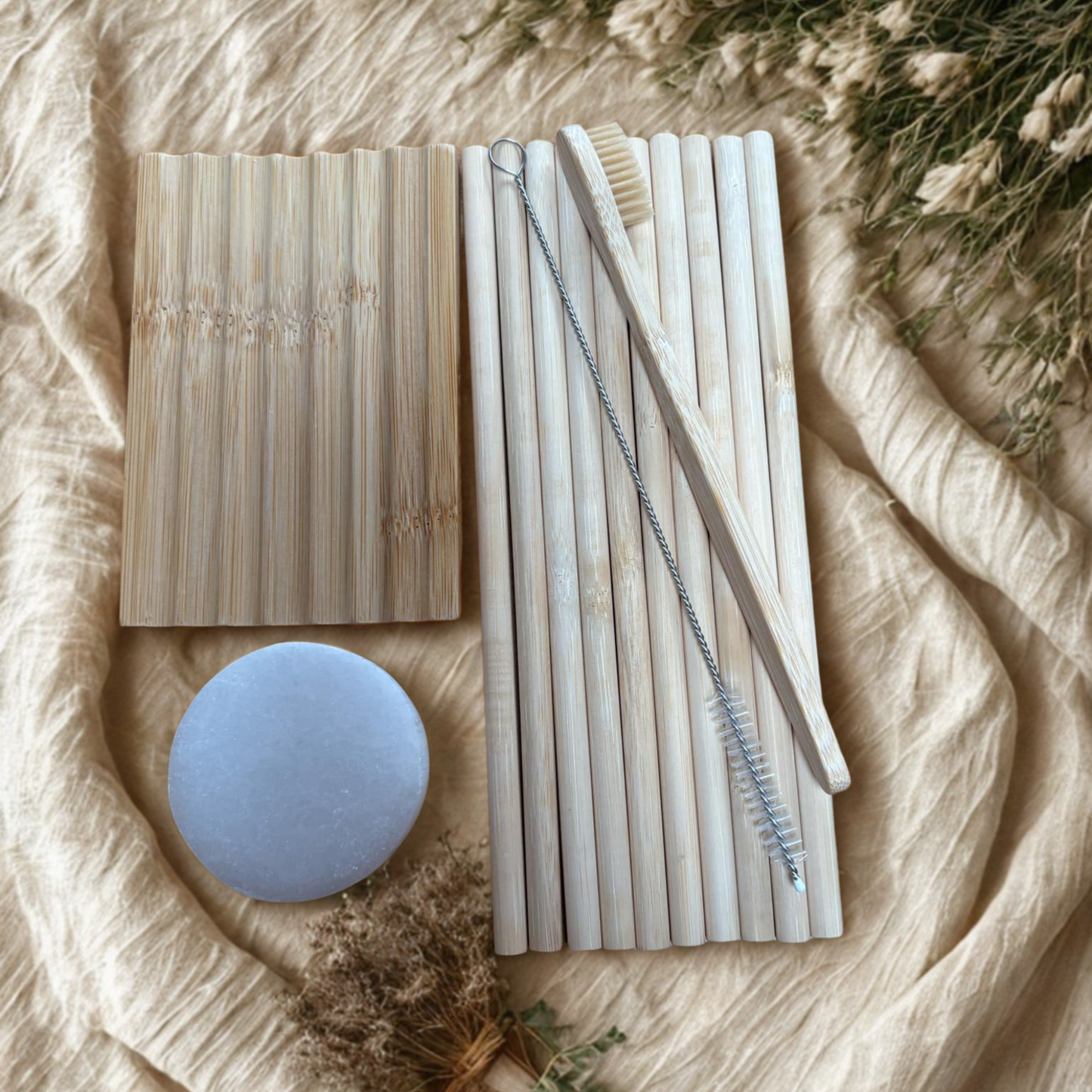 Set of bamboo straws, a cleaning brush, adult bamboo toothbrush, wooden soap dish and selenite charging plate on beige fabric background.