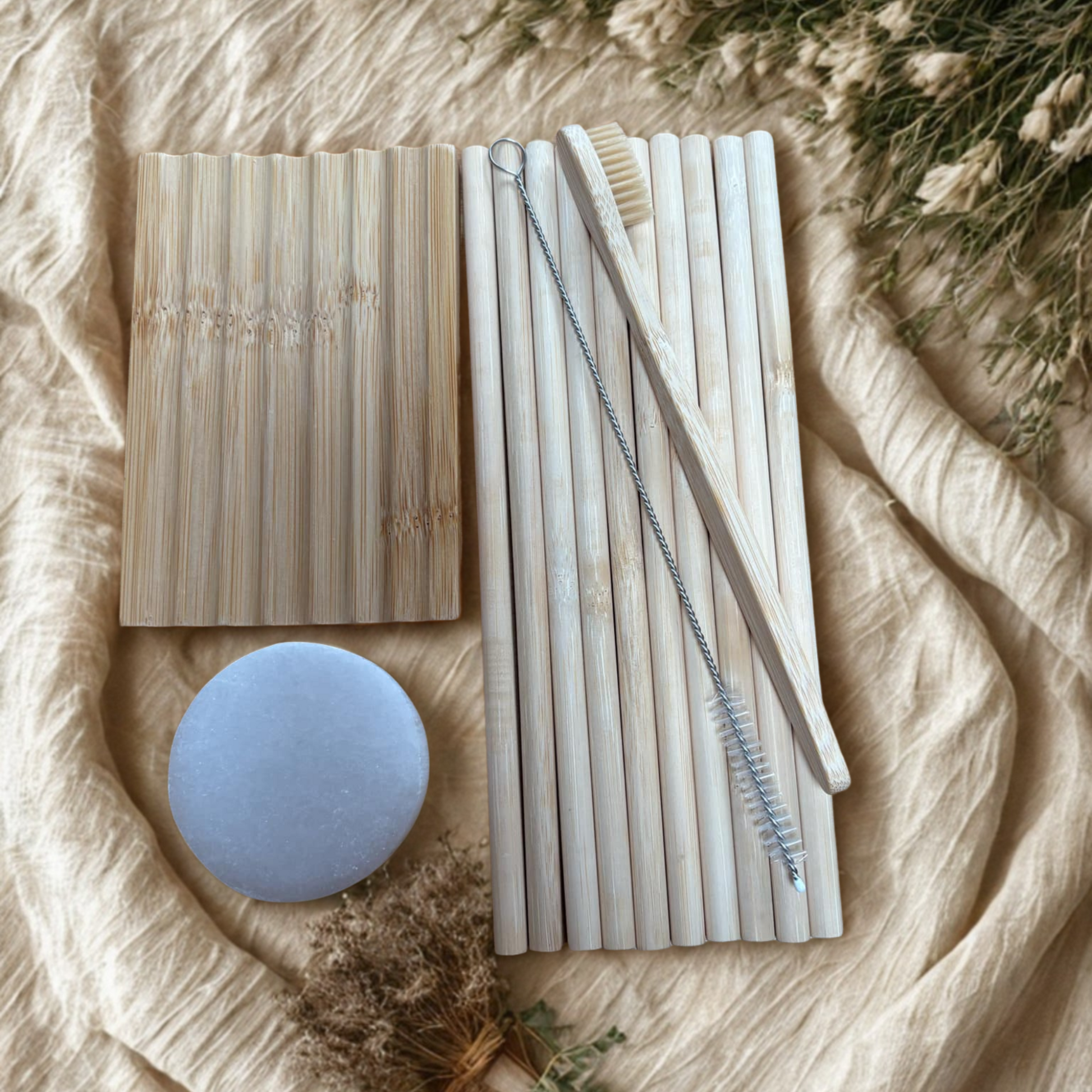 Set of bamboo straws, a cleaning brush, adult bamboo toothbrush, wooden soap dish and selenite charging plate on beige fabric background.