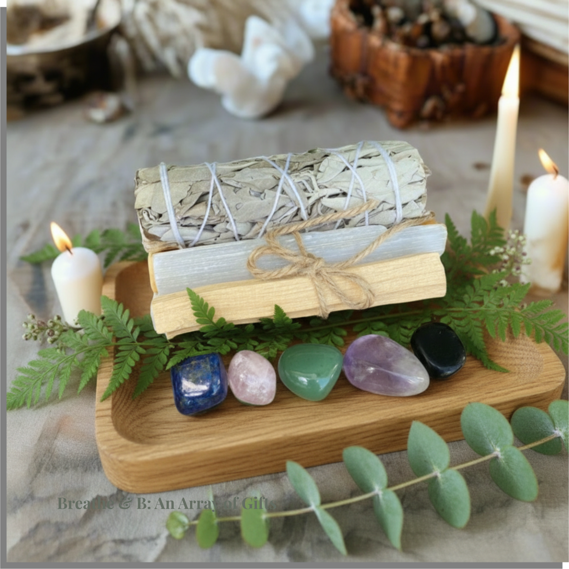 Smudge, selenite, palo santo and crystal tumble stone on a wooden tray surrounded by candles and greenery