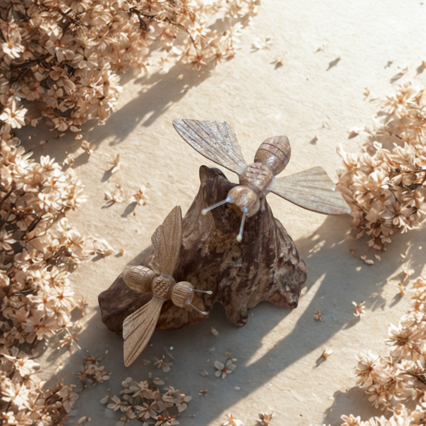 Two bees sitting on driftwood surrounded by dried flowers on a light surface