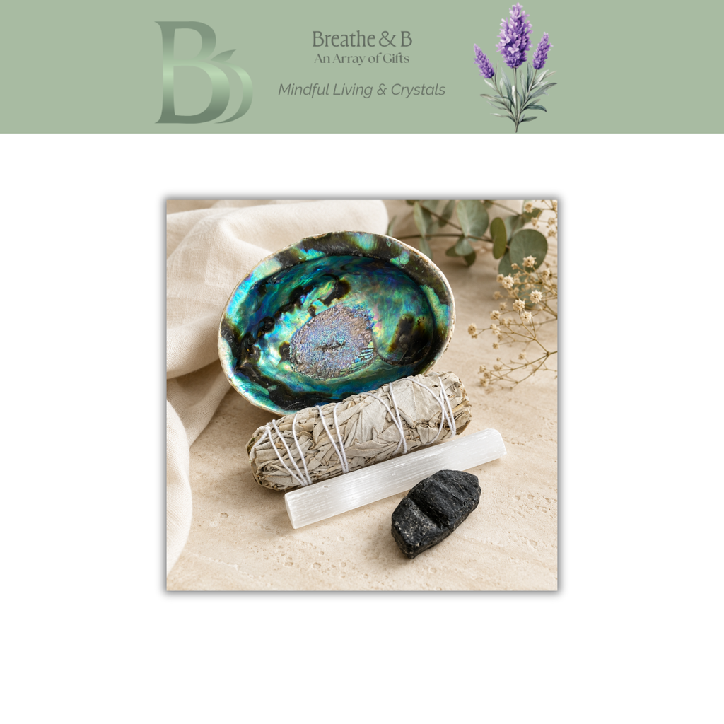 A square product presentation featuring a decorative abalone shell dish with a blue and green iridescent interior, styled with a sage smudge bundle, white crystal, and black stone on a beige surface. The image is framed by a light green header with the brand logo 'Breathe & B' and the text 'An Array of Gifts' and 'Mindful Living & Crystals'.